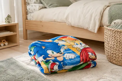 Plaid polaire multicolore Sonic plié au pied d’un lit d’enfant en bois clair