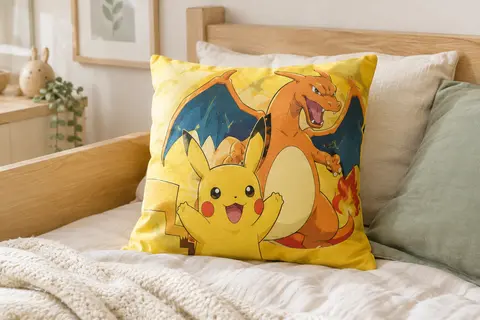 Coussin carré jaune Pokémon Pikachu et Dracaufeu posé sur un lit d’enfant aux tons crème