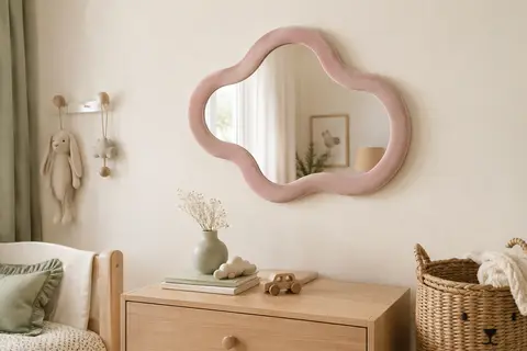 Miroir mural rose en forme de nuage, à finition veloutée, suspendu au-dessus d’une commode en bois clair.