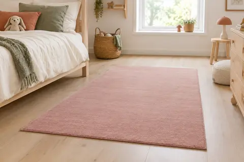 Tapis rectangulaire rose à poils ras posé sur un parquet clair dans une chambre d’enfant lumineuse