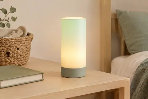 Lampe de chevet LED cylindrique RGB posée sur une table en bois clair dans une chambre d’enfant